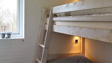 A bunk bed with a ladder, a window with two cups on the sill, and a wall-mounted light.