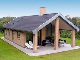 A modern house with a sloped roof, a covered patio area with outdoor furniture, and a brick chimney.