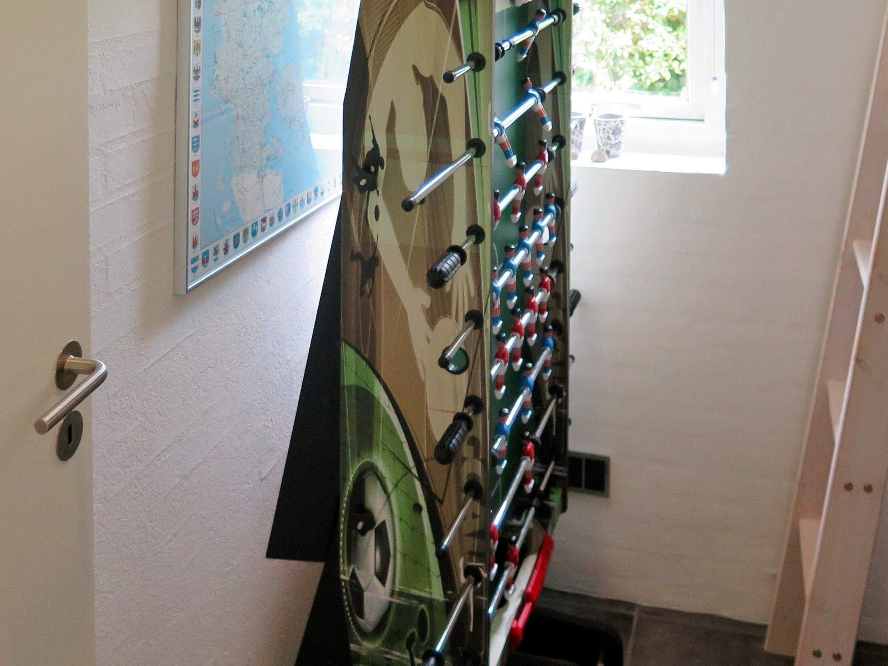 Ein Zimmer mit Kicker, einer Karte an der Wand und einem Fenster mit Blick auf Grünflächen.