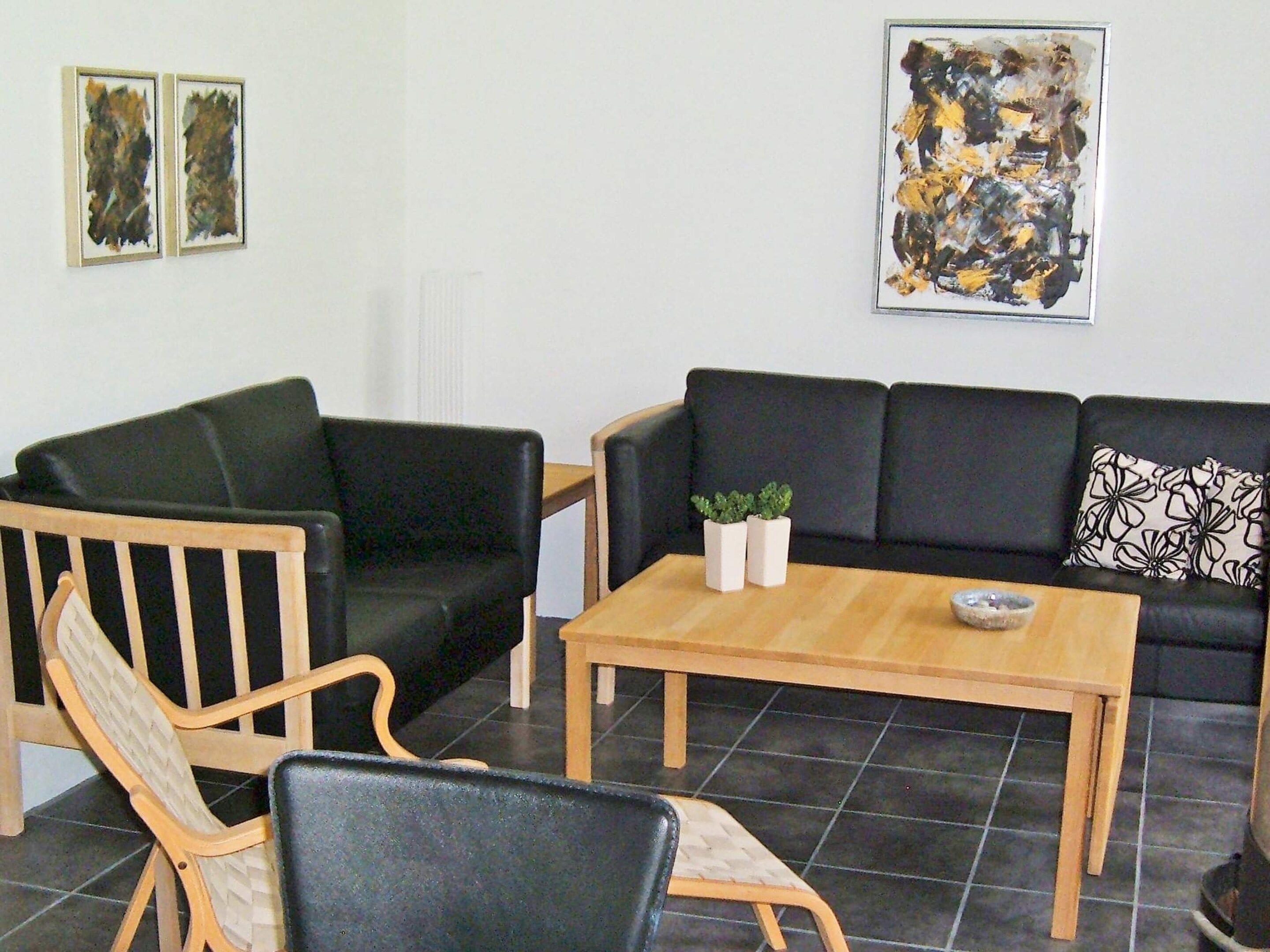 A living room with a black sofa, wooden armchairs, a coffee table, and two framed artworks on the wall.