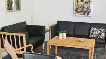 A living room with a black sofa, wooden armchairs, a coffee table, and two framed artworks on the wall.