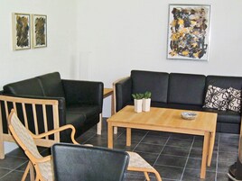 Una sala de estar con un sofá negro, sillones de madera, una mesa de centro y dos cuadros en la pared.