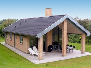 A modern house with a covered patio, a brick chimney, and a glass door leading to an outdoor seating area. - 4 Star Holiday Home in Struer (Struer)