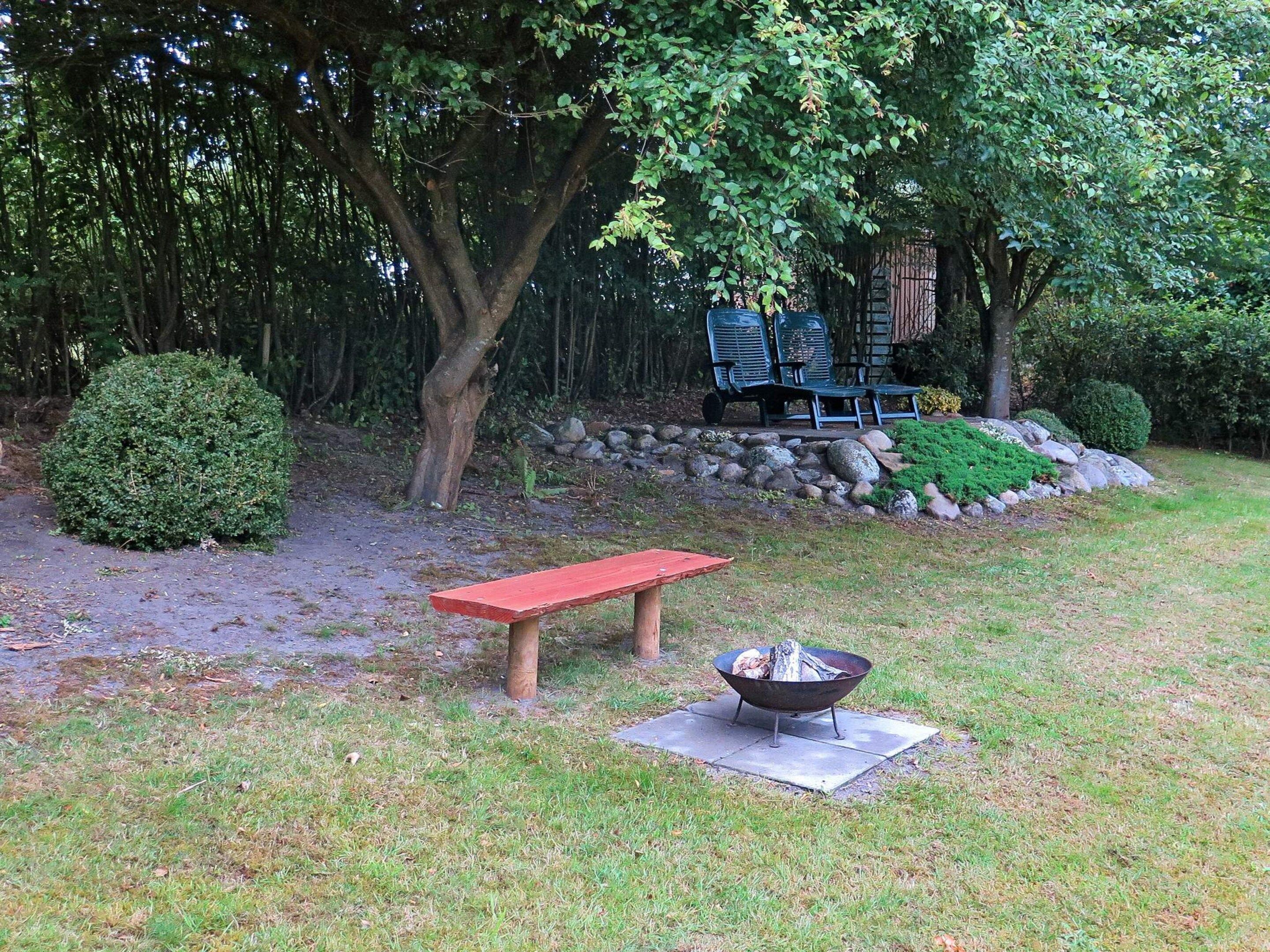 A garden with a red bench, a fire pit, and a stone wall with greenery.