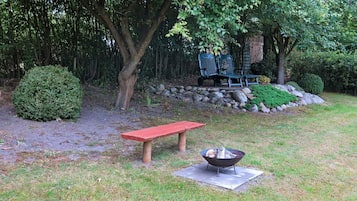 Un jardí amb una bosa vermella, una xemeneia i una paret de pedra amb vegetació.