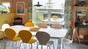 Un comedor con una mesa y sillas blancas, una ventana con cortinas y vista a la vegetación exterior.