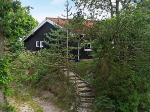 Una casa con facciata scura, circondata da vegetazione fitta e una scala in legno che conduce all'ingresso.