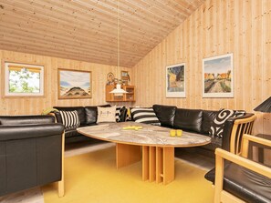 A cozy room with a wooden ceiling, a round table, leather sofas, and framed pictures on the walls.