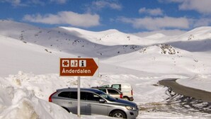 Paisatge nevós amb carretera, un senyal que indica Anderdalen i cotxes estacionats.