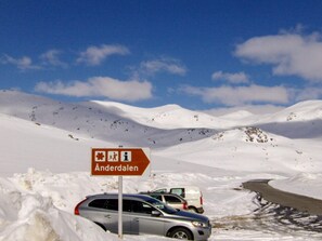 Un paysage enneigé avec une route, un panneau indiquant Anderdalen et des voitures garées.