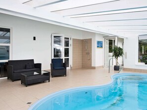 Un espace piscine doté d’une douche en verre, de meubles en osier et d’une plante en pot.
