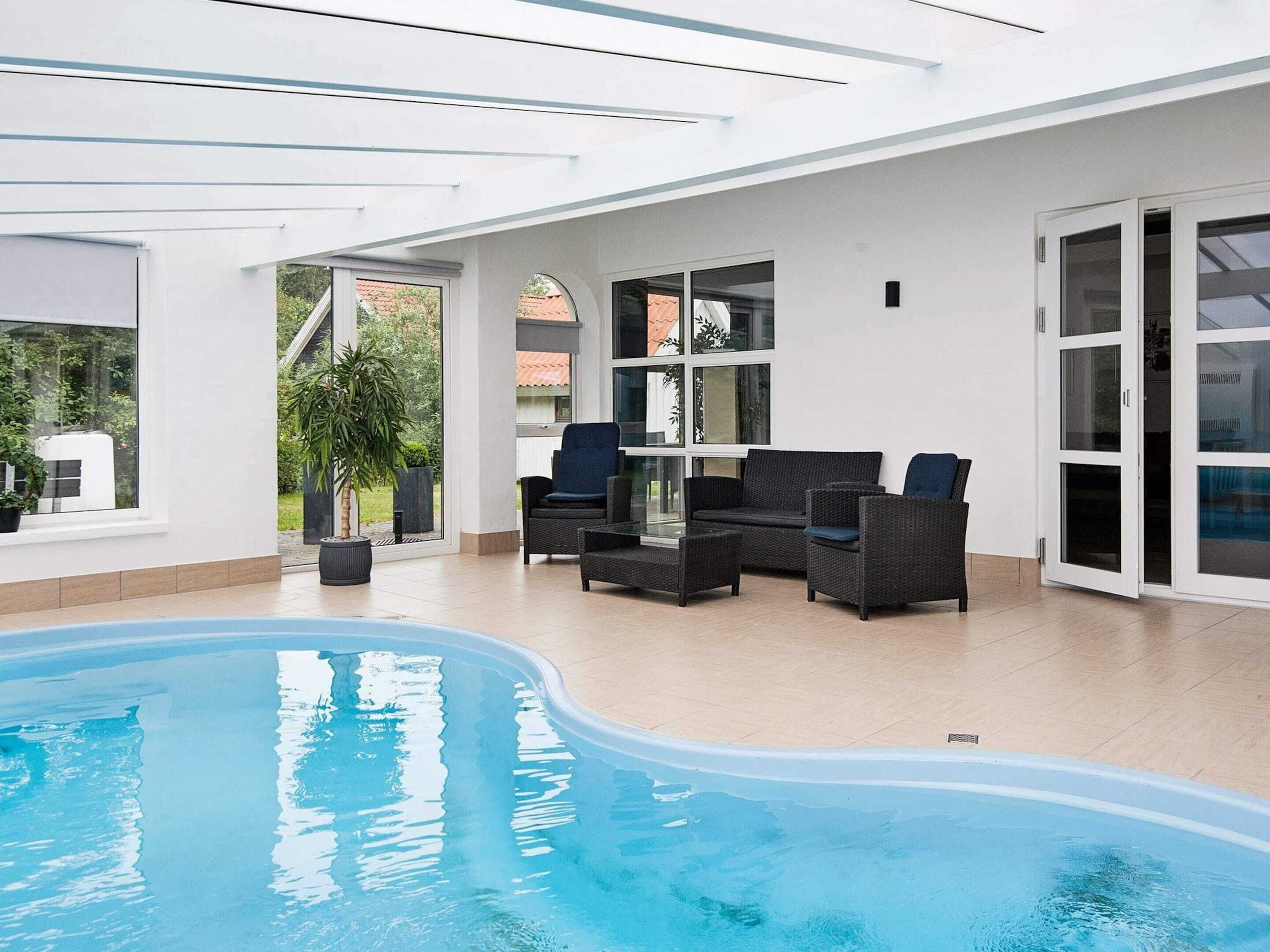 A swimming pool with a sunlit patio area, outdoor furniture, and a view of the surrounding landscape.