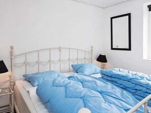Un lit avec un cadre en métal blanc et une literie bleue, deux lampes de chevet et un miroir au mur.
