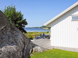 A wooden deck with outdoor furniture overlooking a body of water and a white building with a window. - 4 Person Holiday Home in Henan (Henån)