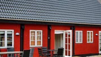 A red building with a tiled roof, white-framed windows, and a wooden deck with outdoor seating.