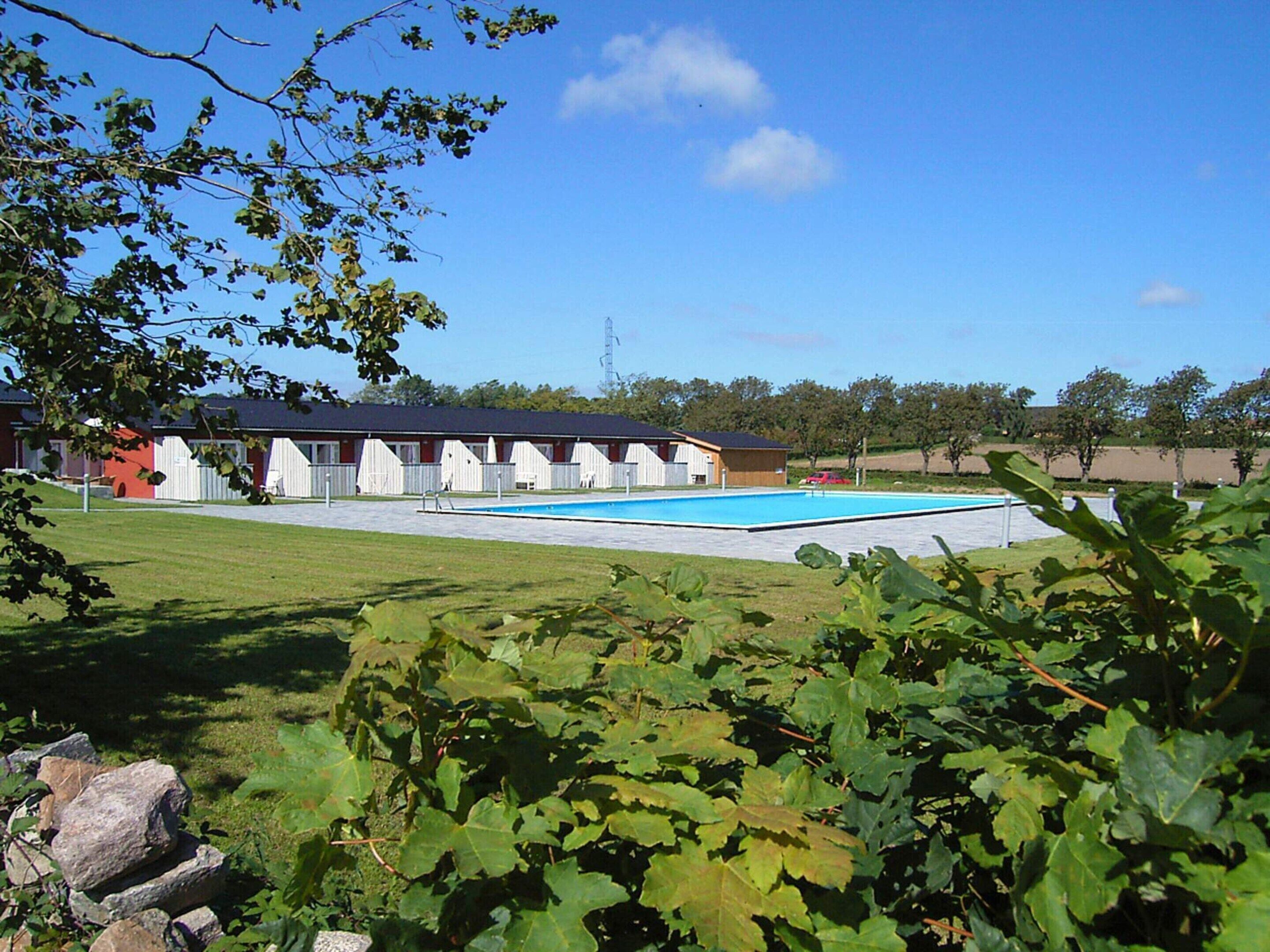 A hotel with a swimming pool, a fenced garden, and a row of single-story buildings.
