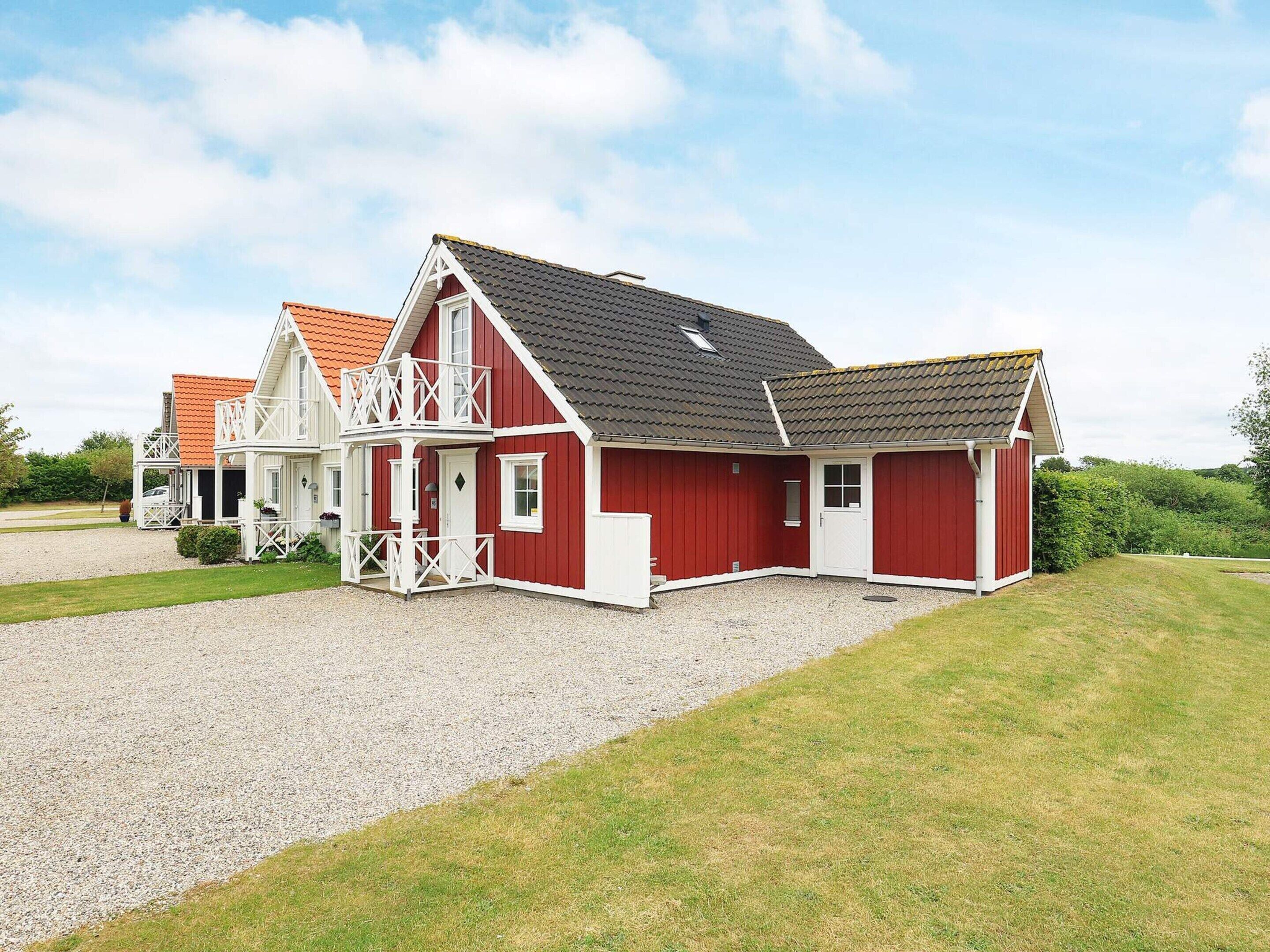 A red and white building with a balcony, a gravel driveway, and a grassy area.