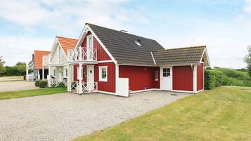 A red and white building with a balcony, a gravel driveway, and a grassy area.