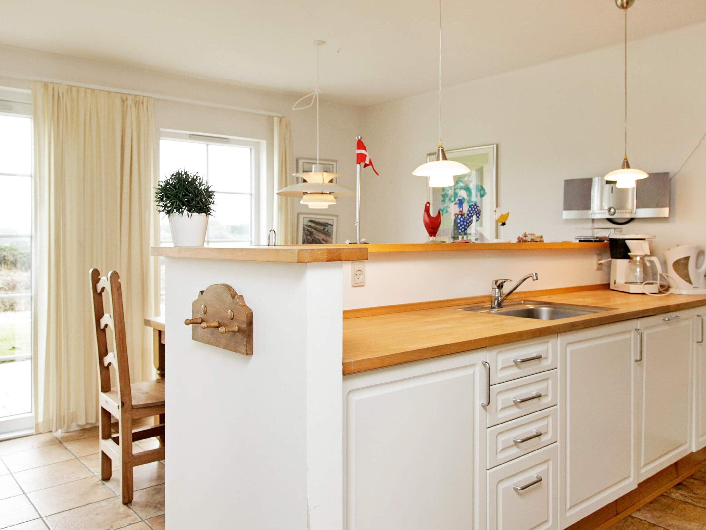 Una cocina con encimera de madera, armarios blancos, un lavabo y una ventana con cortinas.