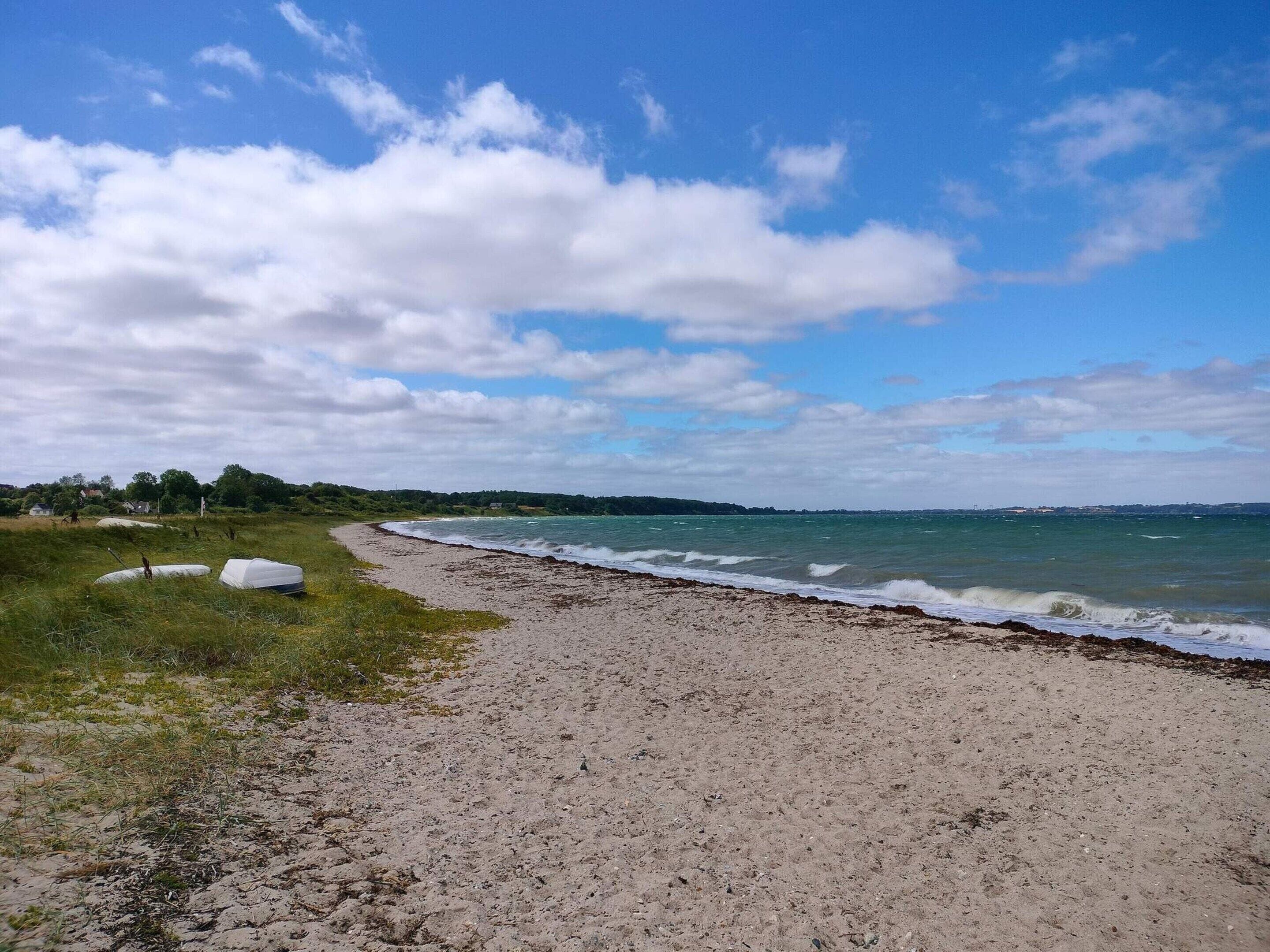 Een strand met een zandstrand, een grasveld en een heldere lucht.