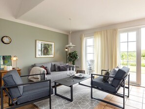 A modern living room with a grey sofa, two armchairs, a coffee table, a floor lamp, a painting, and a large window with curtains. - 8 Person Holiday Home in Brenderup Fyn (Middelfart)