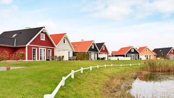 Una hilera de casas con fachadas rojas y blancas, un área con césped y un pequeño estanque.
