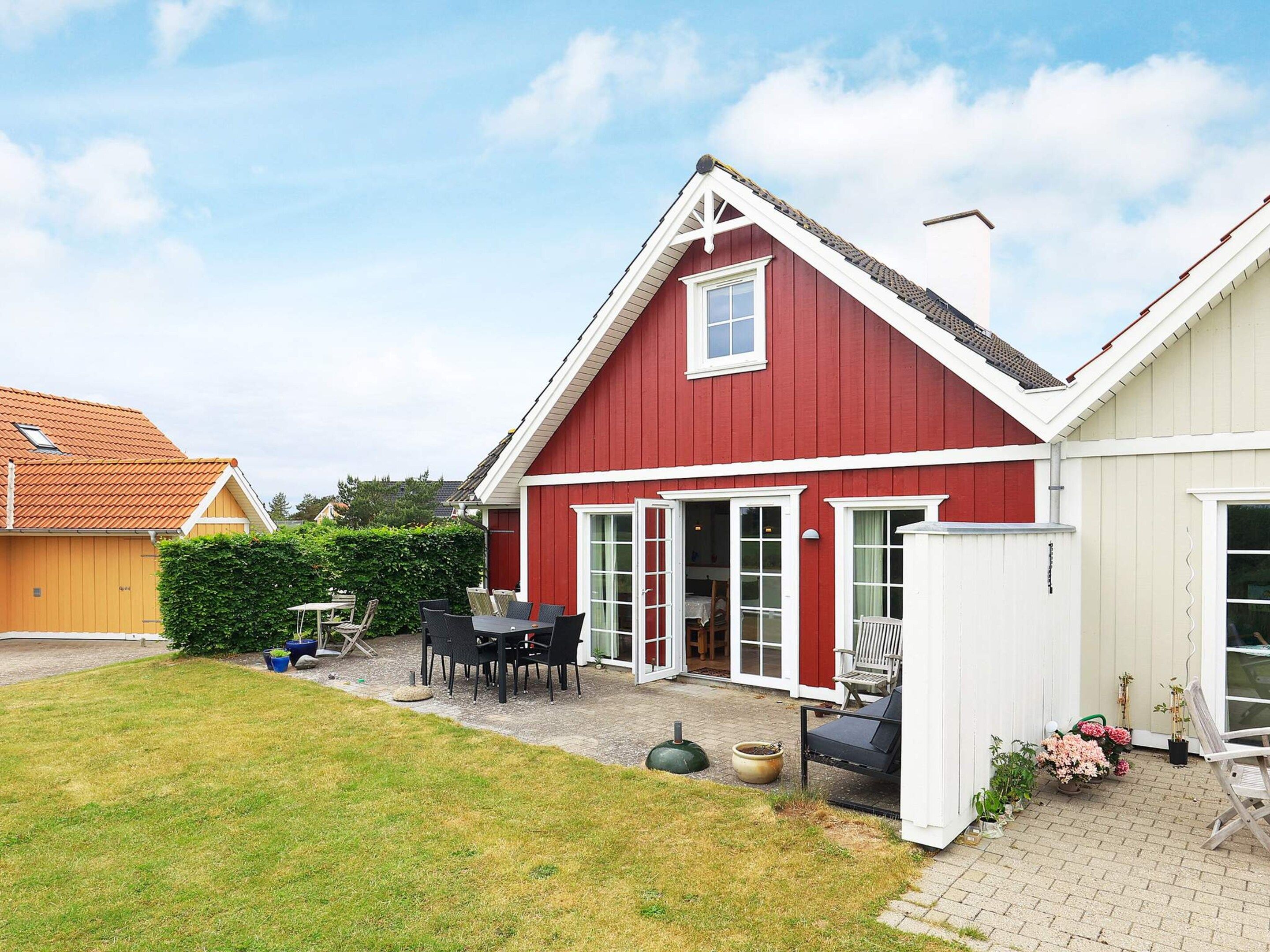 Et rødt hus med hvide døre og vinduer, en terrasse med stole og et lille haveområde.