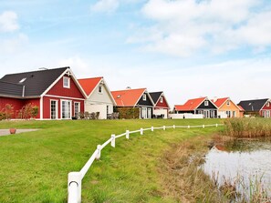 Una hilera de casas rojas y blancas con una cerca blanca y un estanque.