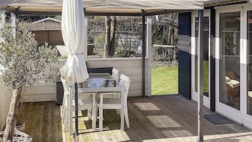En overdækket terrasse med et bord, stole, en hvid parasol og en potteplante.