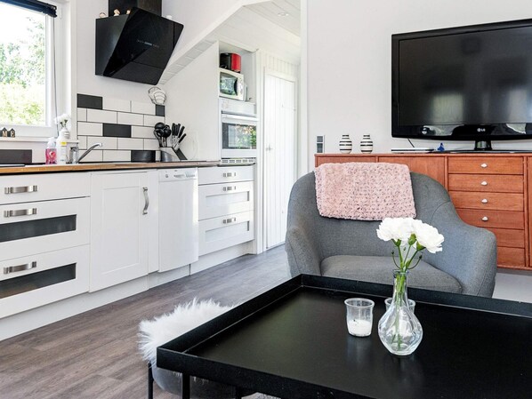 A modern kitchen with white cabinetry, a black countertop, and a grey armchair with a pink throw.