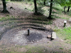 A forested area with a circular stone structure, possibly a well or a pond, surrounded by a gravel path. - 4 Person Holiday Home in Hovborg (Hovborg)