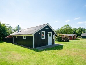 A small, single-story building with a dark exterior and a white door, surrounded by a grassy area and trees. - 4 Person Holiday Home in Hovborg (Hovborg)