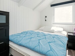 A bedroom with a bed, a nightstand, a dresser, a window, and a wall-mounted lamp.
