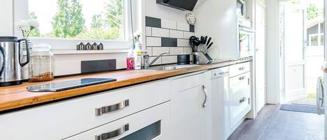 A modern kitchen with white cabinetry, a wooden countertop, and a black range hood.