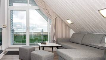 Une chambre de style loft moderne, dotée d’une grande fenêtre, d’un canapé, de poufs et d’une petite table.