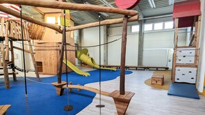 A play area with wooden climbing structures, a slide, and soft flooring.