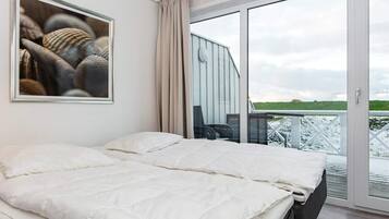 Et soveværelse med en stor seng, udsigt til det fri gennem en skydedør og et billede i ramme på væggen.