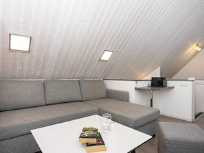 Camera da letto loft moderna con soffitto a falde, un divano grigio, un piccolo tavolo bianco con libri e bicchieri, e un angolo cottura.