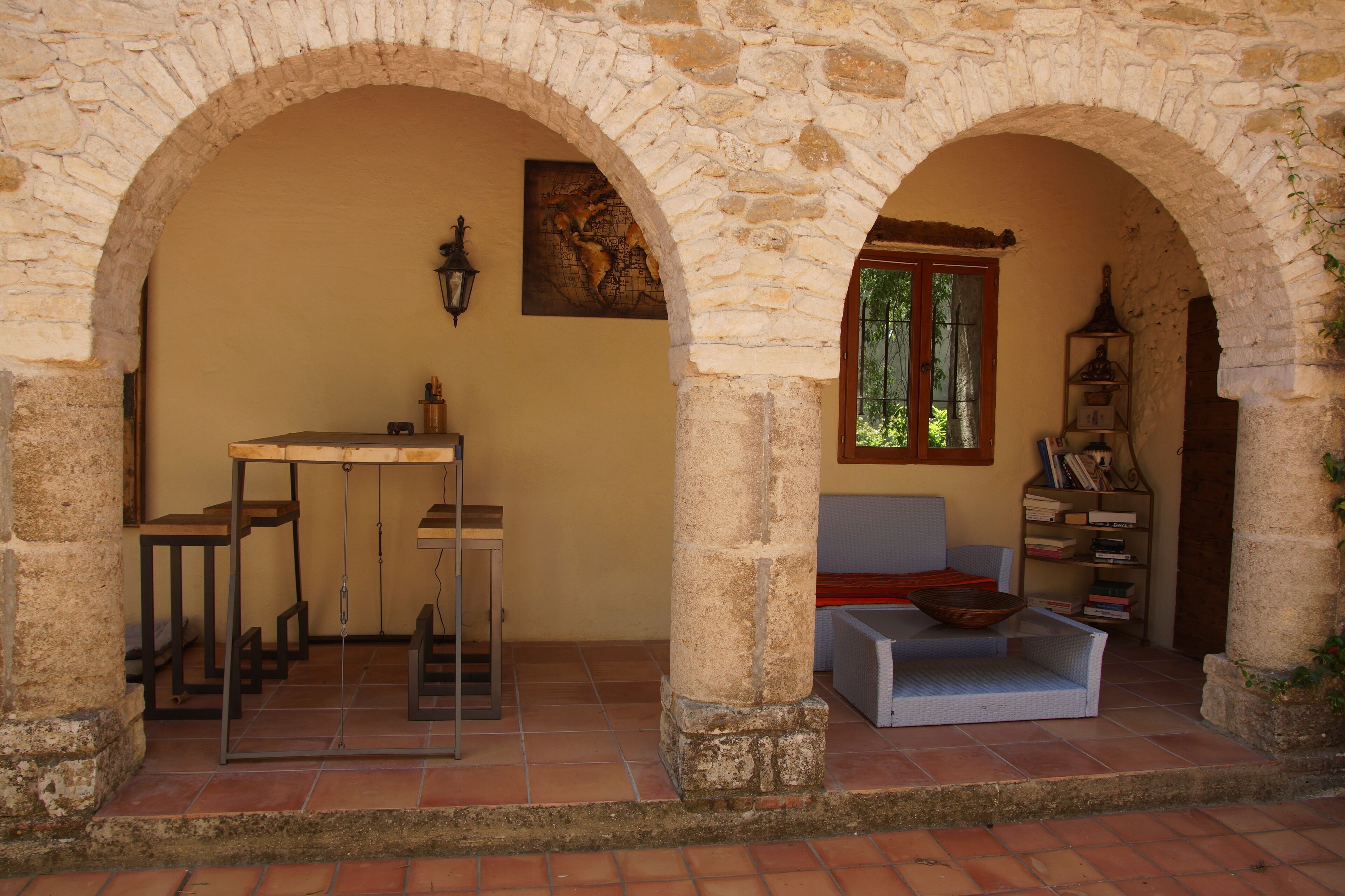 Ein gepflasterter Innenhof mit Tisch und Stühlen, einer Polster-Sitzgruppe und einem Bücherregal.