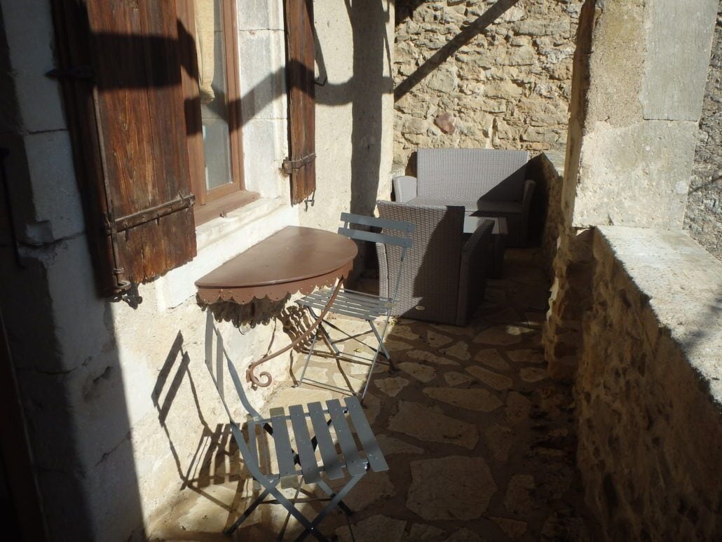 Un patio con suelo de piedra, una mesa y sillas, una silla de mimbre y una puerta de madera.