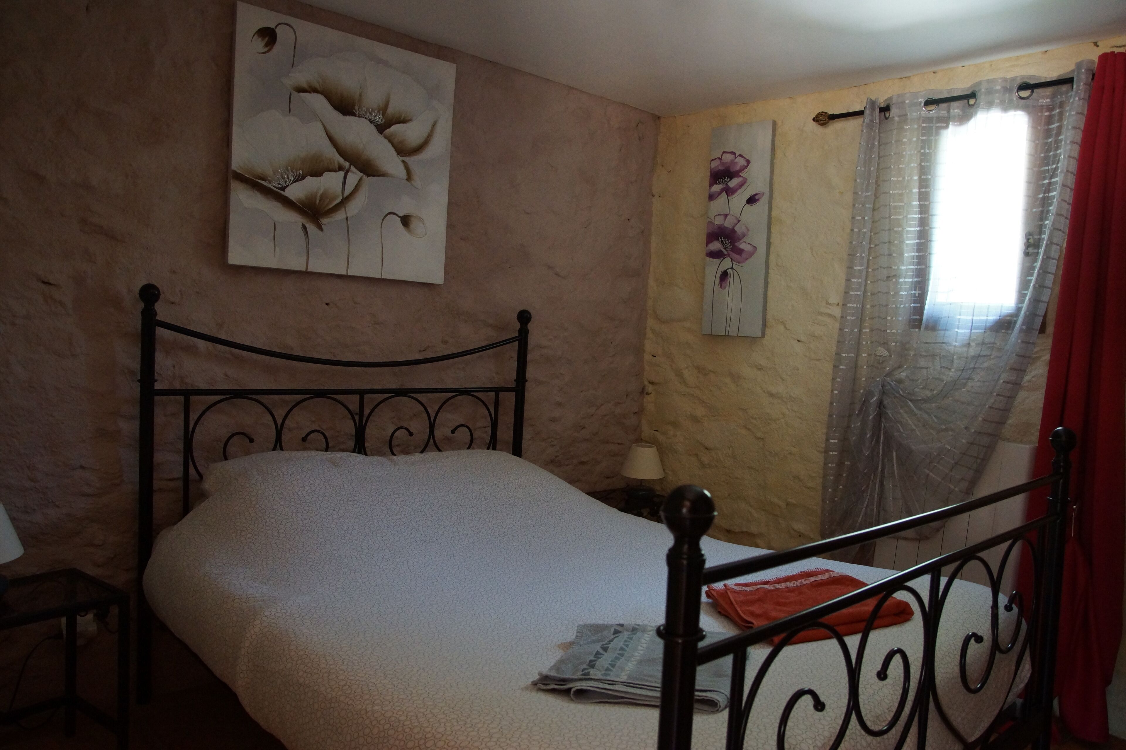 Un dormitorio con una cama individual, un cuadro colgado en la pared, una ventana con cortina y una mesita de noche con lámpara.