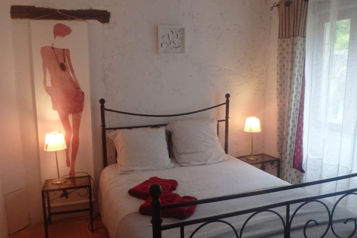 A bedroom with a single bed, two bedside tables, a wall-mounted artwork, and a window with curtains.