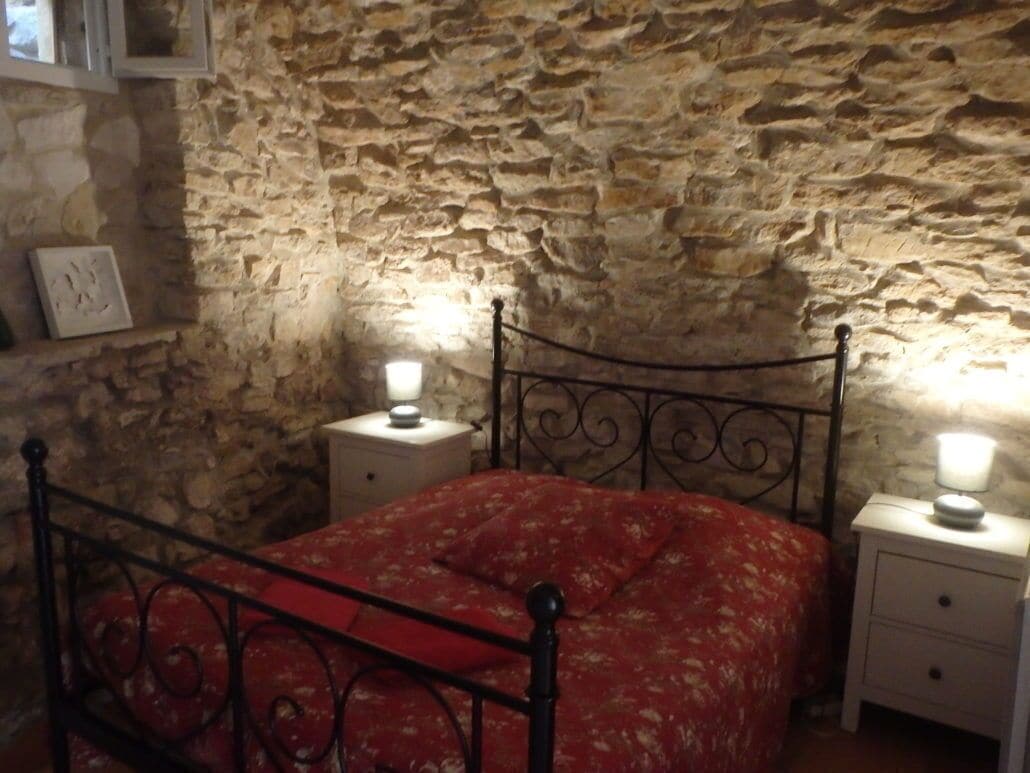 A bedroom with a stone wall, a metal bed frame, and bedside tables with lamps.