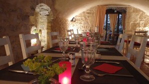 A dining table set with wine glasses, plates, and cutlery, in a stone-walled room with a candle and a view of the outdoors. - Prieuré d'orniols (Goudargues)