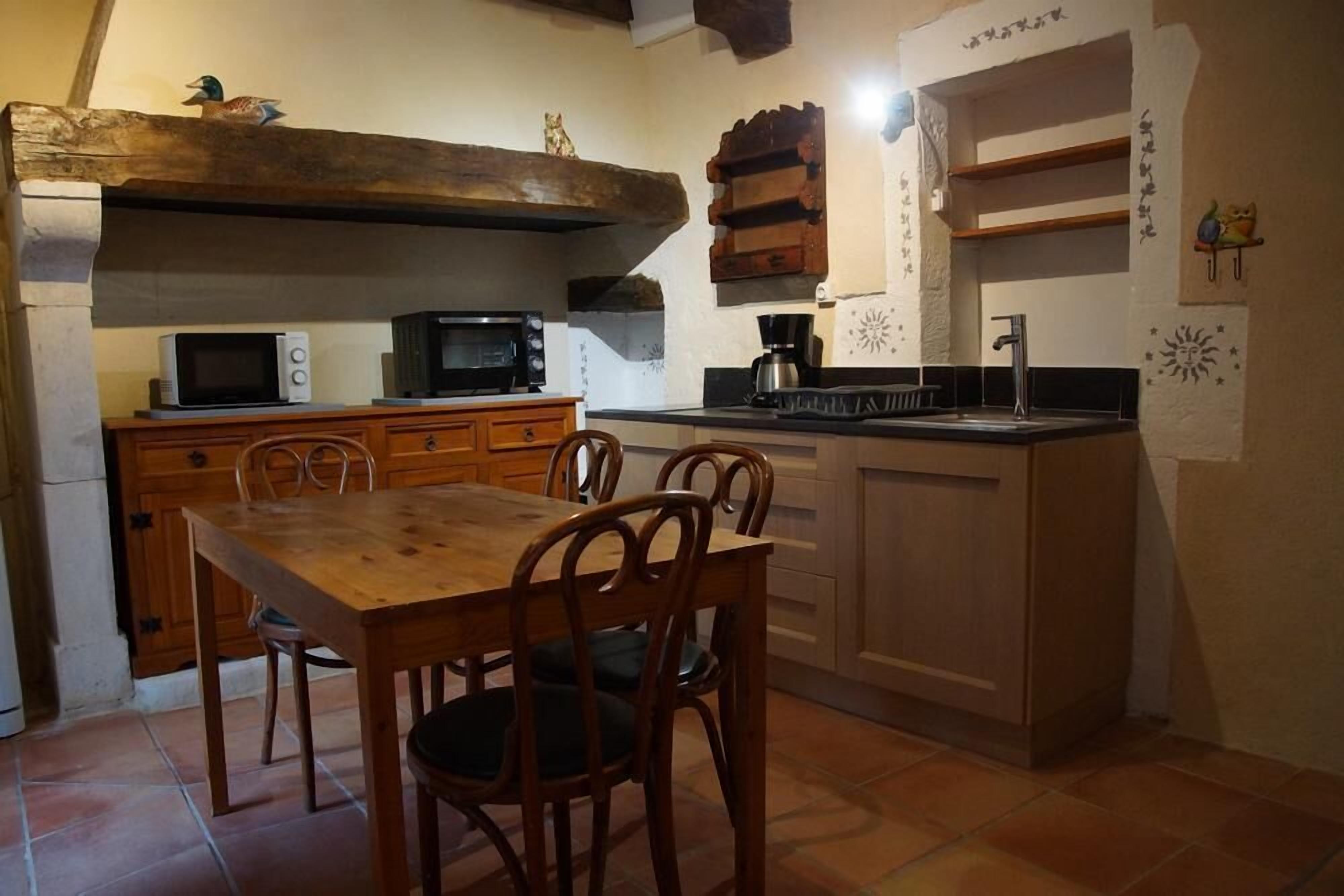 A compact kitchen with wooden cabinets, a dining table with chairs, a microwave, a coffee maker, and a sink.