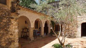 A stone courtyard with arches, outdoor seating, and a tree. - Prieuré d'orniols (Goudargues)