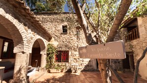 A stone building with arches, a signboard, and a tree. - Prieuré d'orniols (Goudargues)