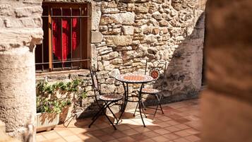 A stone building with a window and a door, a tiled patio with a table and chairs, and a potted plant.