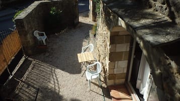 Um edifício de pedra com um pequeno pátio, incluindo uma mesa de madeira e duas cadeiras de plástico branco.