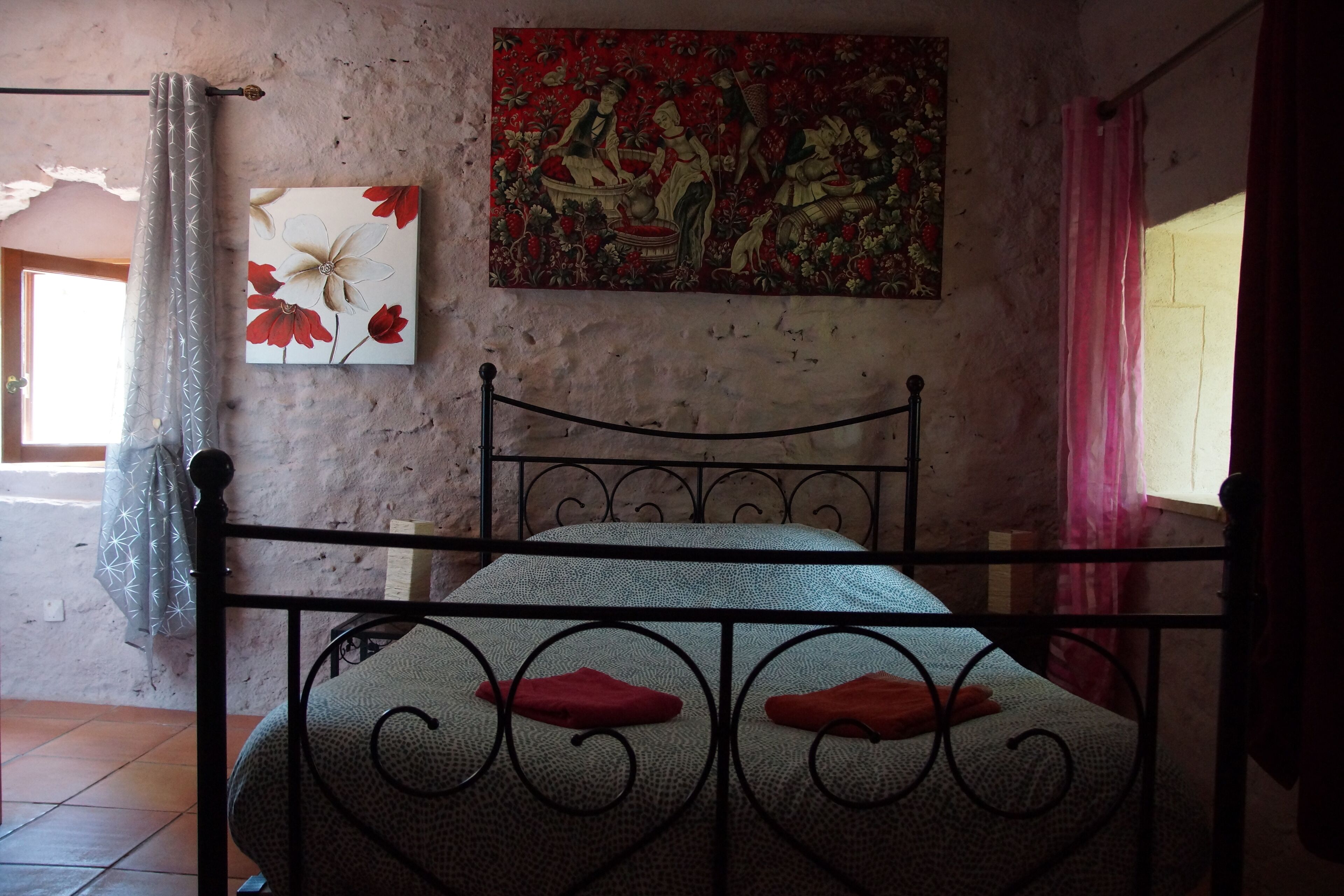 A room with a bed, a painting, and a window with curtains.